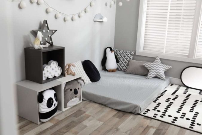 Un lit au sol enfant 70x140 avec une literie grise et des peluches d'animaux, dans une chambre au style scandinave avec des guirlandes lumineuses.
