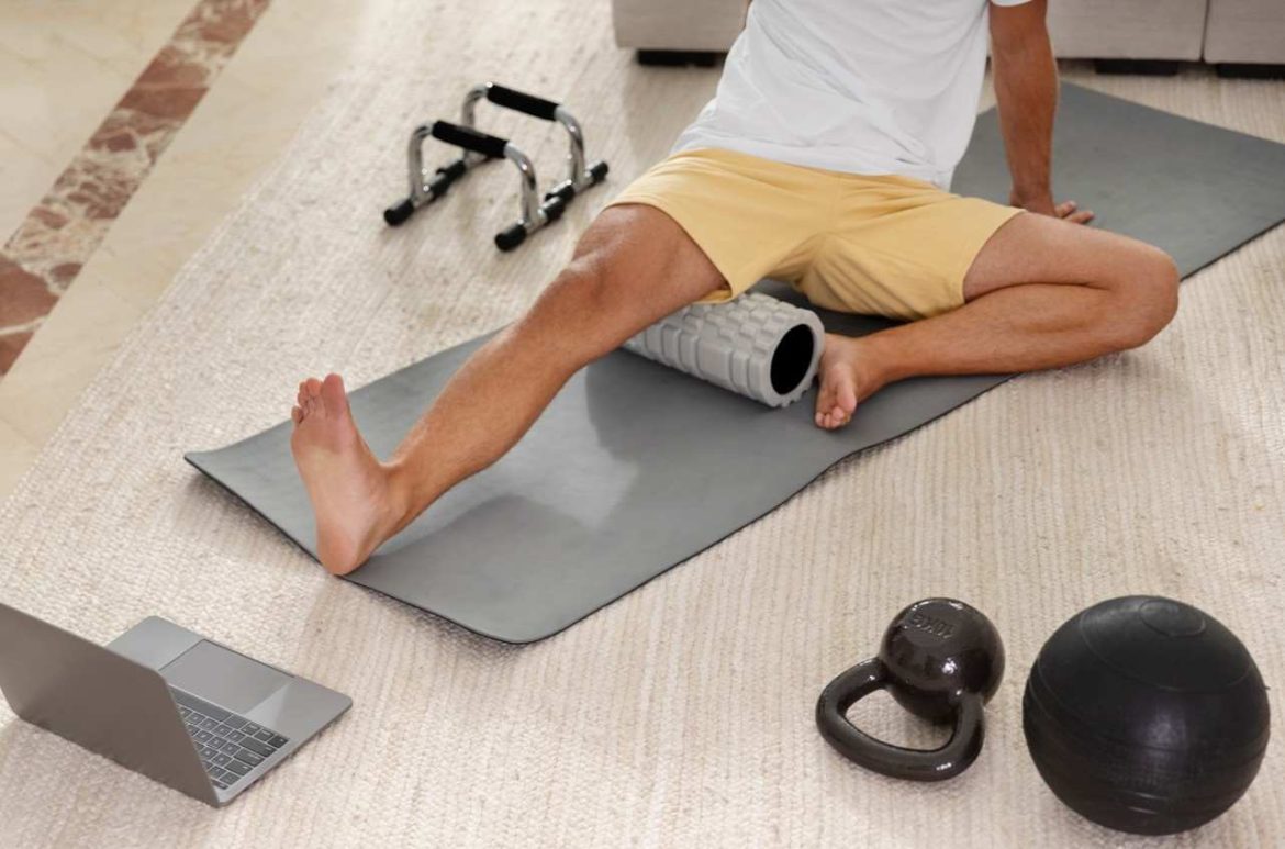 Un homme utilise un rouleau en mousse texturé, l'un des accessoires auto massage efficace domicile, pour détendre les muscles de sa legère jambe sur un tapis d'exercice.