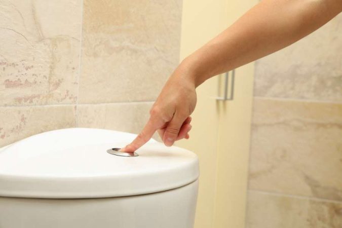 Une main appuie sur le bouton de la chasse d'eau situé sur le couvercle d'un réservoir de toilettes blanc.